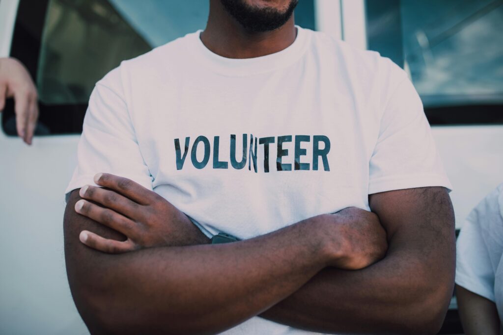 pexels-photo-6646852-6646852 A close-up of a person wearing a volunteer shirt with arms crossed, promoting community service.